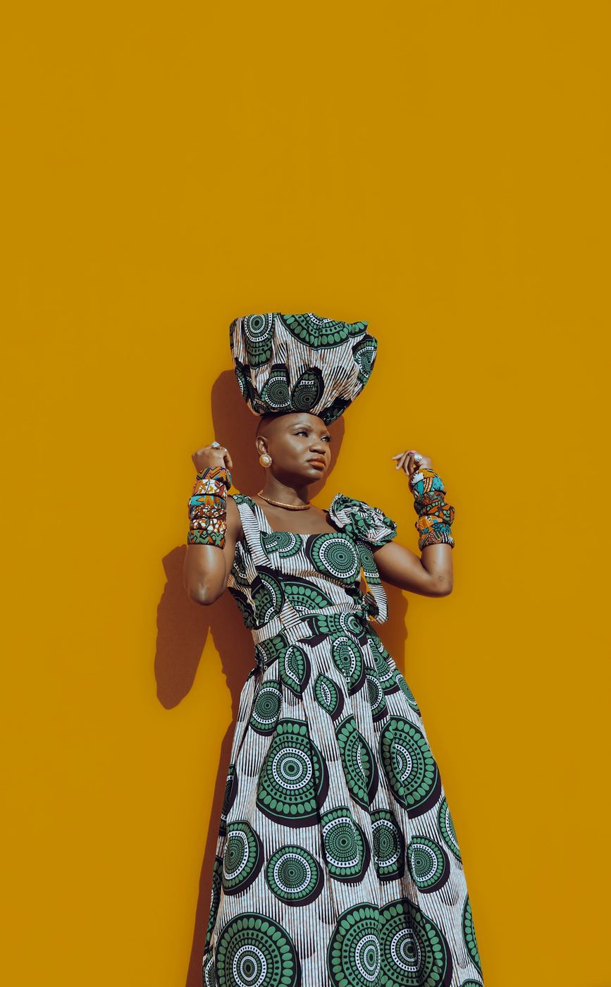 Customer wearing a dress and hat against a painted wall